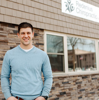 Photo of chiropractor Jeff Redenius, a young male in a light blue sweater, standing in front of his chiropractic office